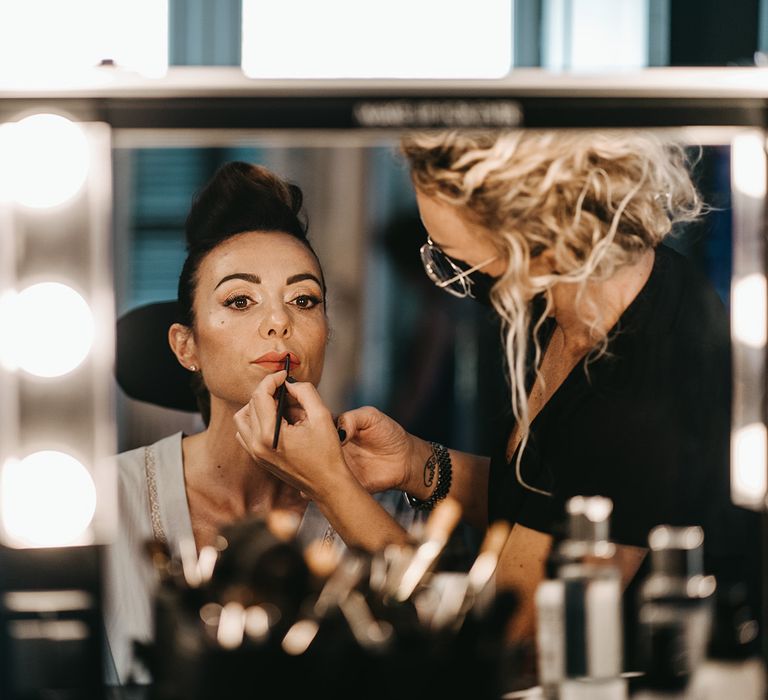 Bride does her lipstick in front of brightly lit mirror on her wedding day