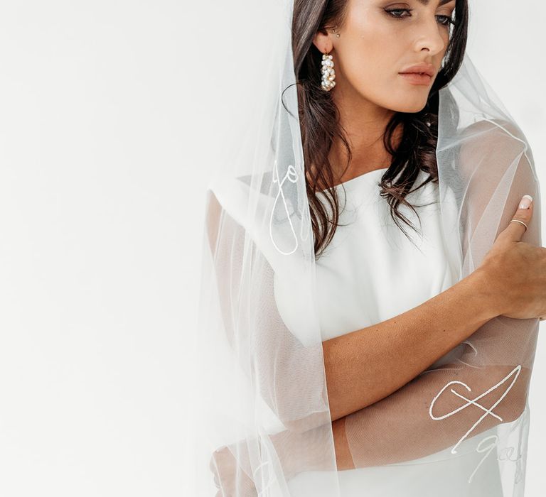 Bride in a fitted wedding dress with a cathedral length veil covered in embroidered words 