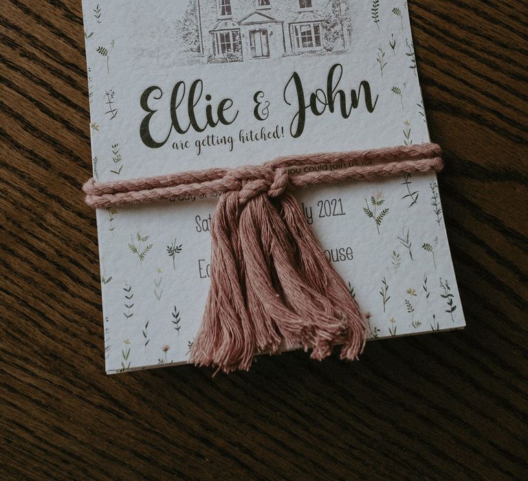 Wedding invite on white paper with house illustration and leaf prints tired with pink rope for Isle of Wight wedding with macrame wedding decor