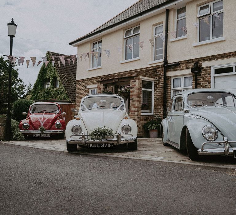 Three VW bugs decorated for wedding with ribbon and florals parked outside house before Isle of Wight wedding with macrame wedding decor