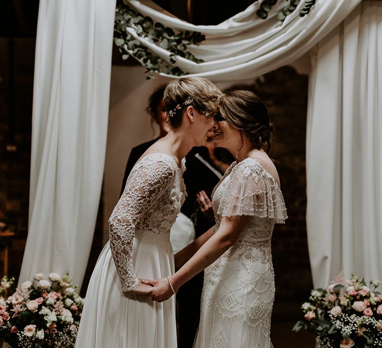 Bride with short hair in an appliqué wedding dress with long sleeves holding hands with her bride at the altar of Woolas Barn in an embellished wedding dress