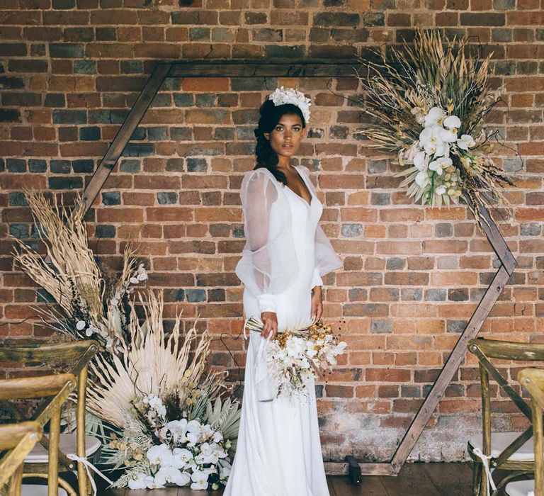 Boho bride in a long sleeve wedding dress standing in front of a hexagonal altar decorated with dried flowers 