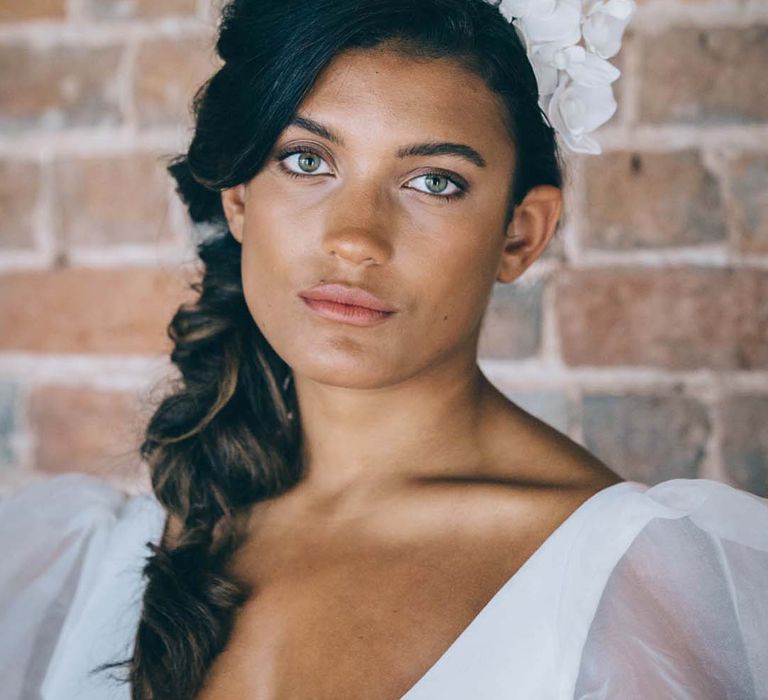 Bride with long dark hair tied in a braid with a white flower headband bridal accessory and natural wedding makeup 