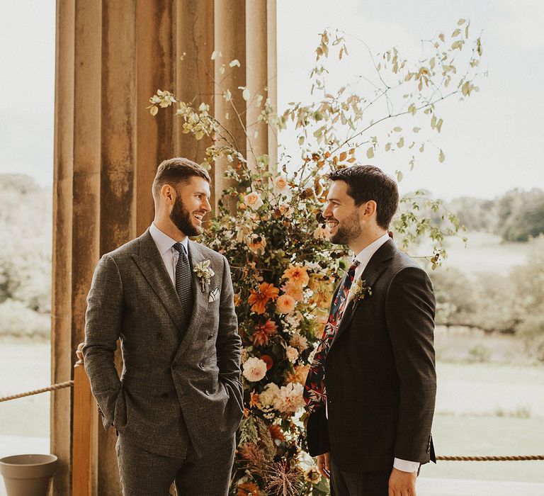 Groom stands with his groomsmen on wedding day as they talk before wedding ceremony