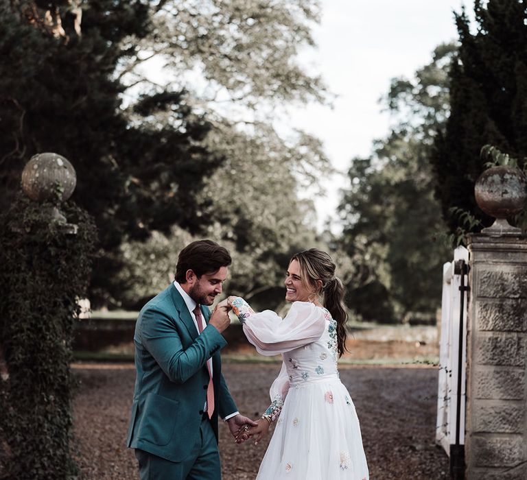 Groom in blue suit and pink tie kisses hand of bride in long mesh sleeve wedding dress with train at Iscoyd Park