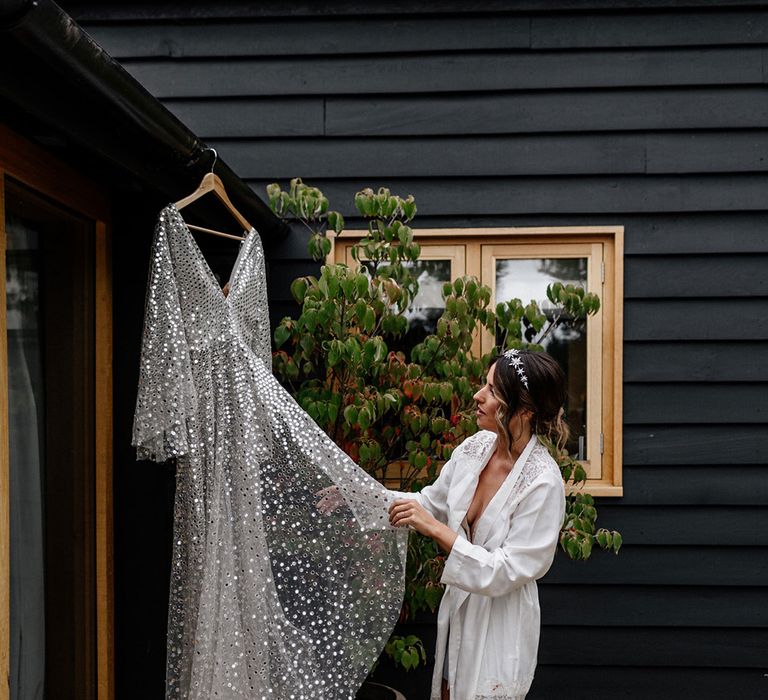 Bride in a satin getting ready robe with lace trim looking at there Silver, sequin, Chosen By Kyha wedding dress 