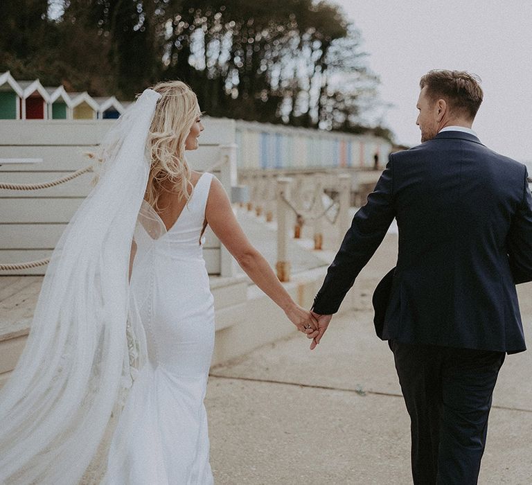 Bride and groom walk hand in hand at coastal wedding