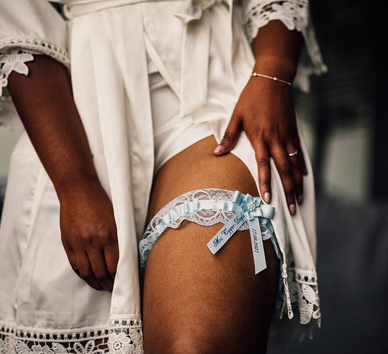 Black bride in a white getting ready robe and something blue wedding garter