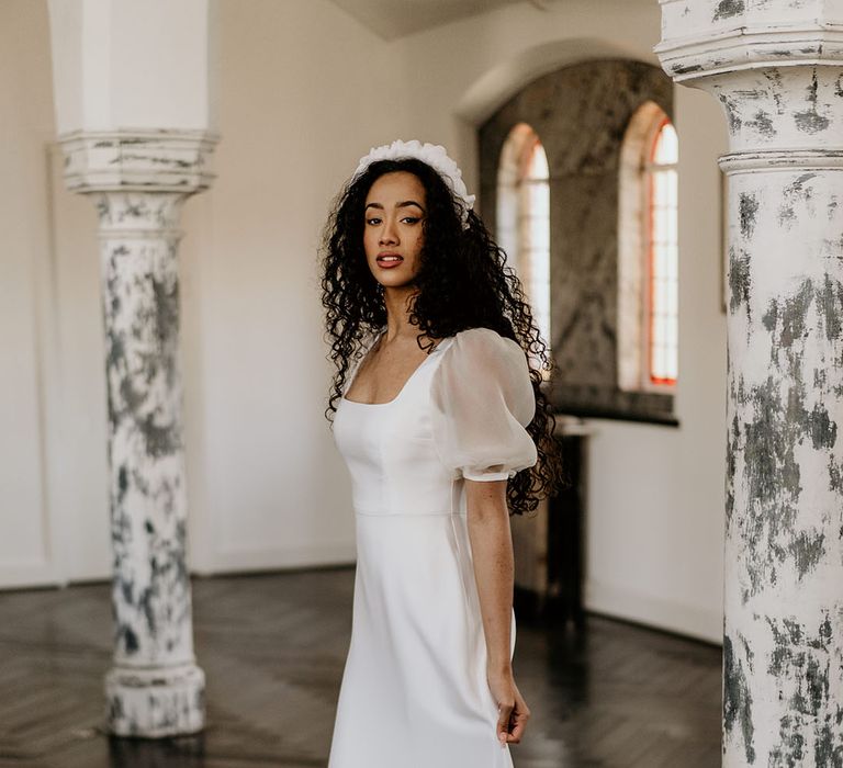 Black bride with long naturally curly hair wearing a headband and A-line wedding dress with puddle train, cap sleeves and square neckline