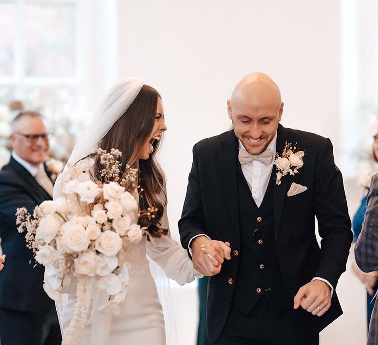 Groom in black wedding suit holding hands with his bride in a long sleeve wedding dress at their Iscoyd Park winter wedding 