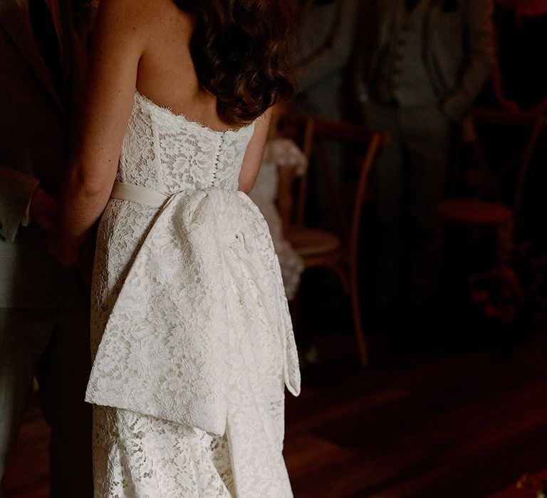 Bride in strapless lace wedding dress with buttons and a large bow and puddle train