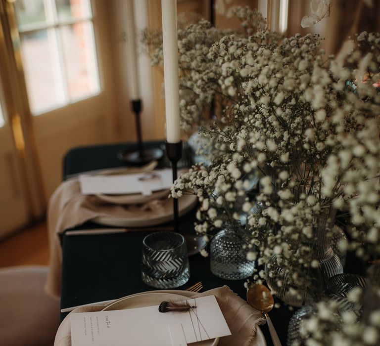 Place setting with black table cloth, gypsophila centrepiece decor and menu cards with feathers 