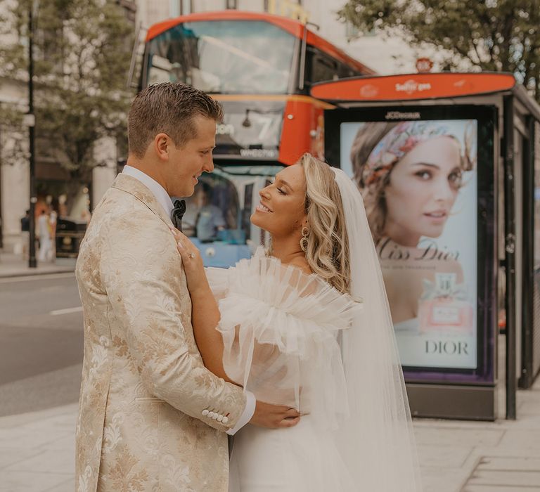 Bride and groom look adoringly at each other as they sand in the busy streets of London together 