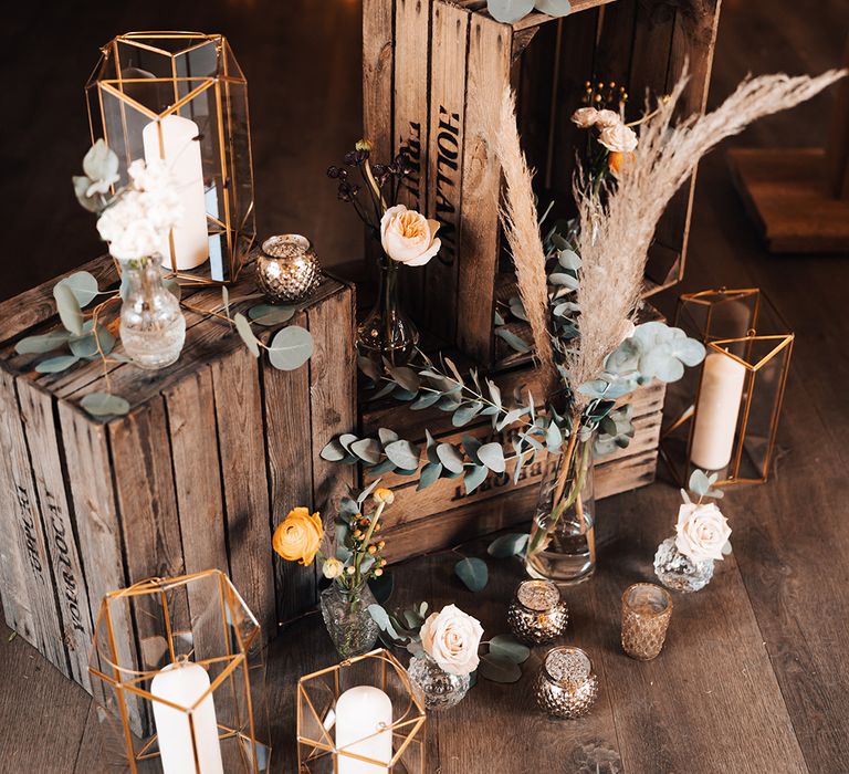 Rustic wedding decor with wooden crates, candles in lanterns and white and orange flowers 