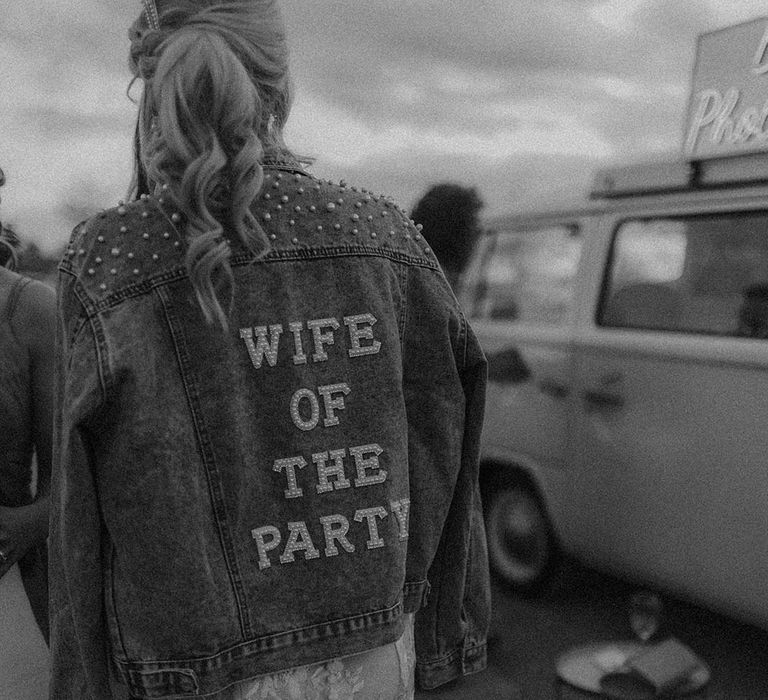 Bride wearing denim jacket embellished with pearls and back reading 'wife of the party' in the evening 