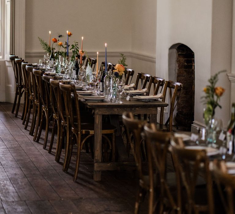 Wooden banquet table with pink, blue, and yellow candles and lots of foliage 