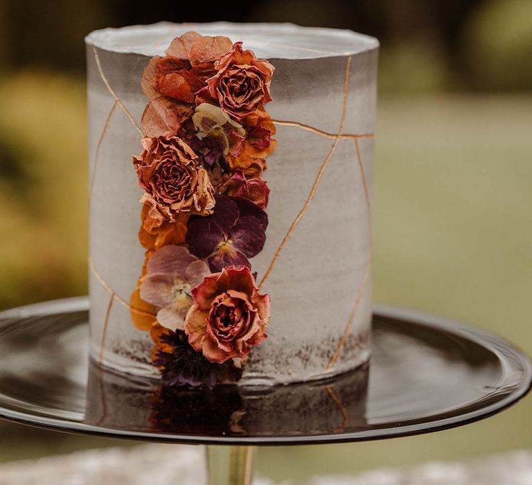 Single tier grey marble effect wedding cake with orange wedding flowers on a black cake stand 