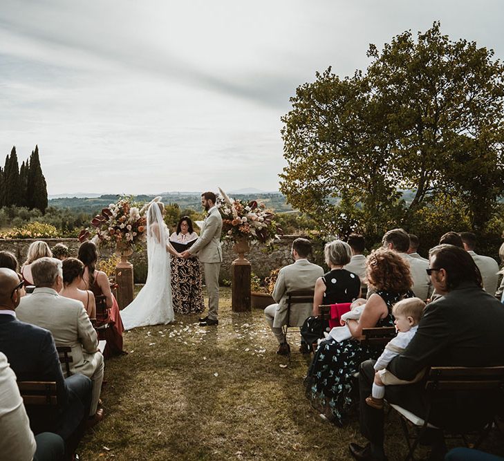 Bride & groom during Tuscan wedding at the Villa Catignano for outdoor wedding ceremony complete with extravagant floral bouquets to the front of aisle 