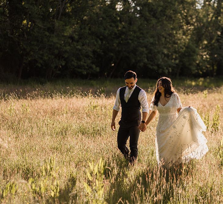 Bride & groom walk through fields during golden hour for couples portraits on wedding day