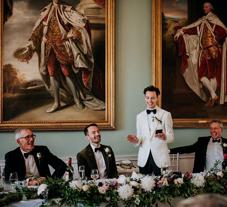 Groom wearing white dinner jacket and white rose buttonhole delivers speech during reception