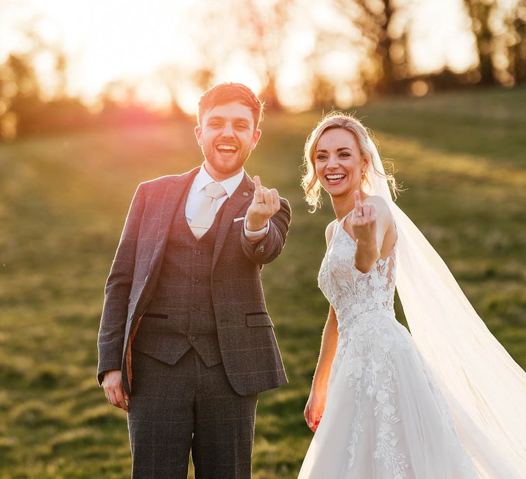 Bride and groom lift their ring fingers to the camera to show off their new wedding bands 