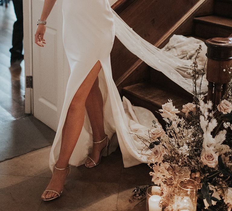 Bride in white satin wedding dress with front slit and embroidered veil with sparkly sandal wedding shoes with pink and white flower decor 