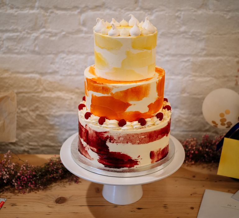 Three tier orange, red and yellow wedding cake finished with white meringue kisses   