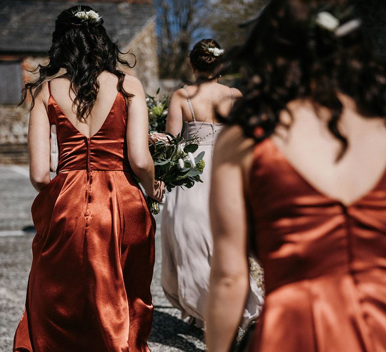 Bridesmaids walk in their orange satin bridesmaid dresses to the ceremony 