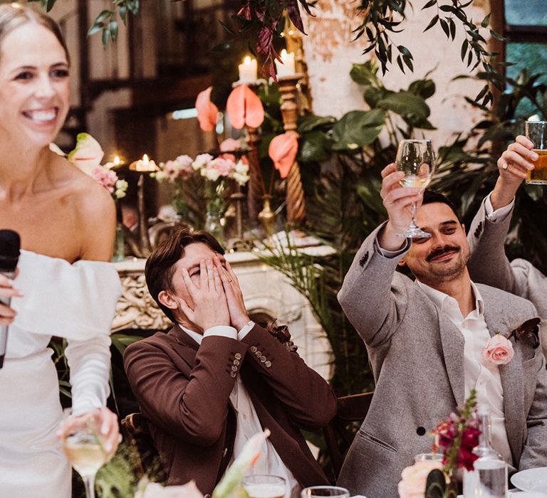 Bride makes a speech as the groom covers his face and the best men raise their glasses