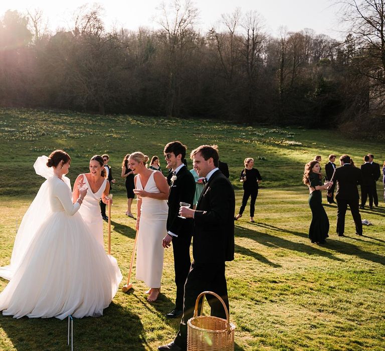 Bride & groom stand on manicured lawns with wedding guests playing croquet 