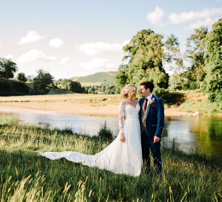 Bride & groom stand in front of lake on their wedding day for couples portraits 