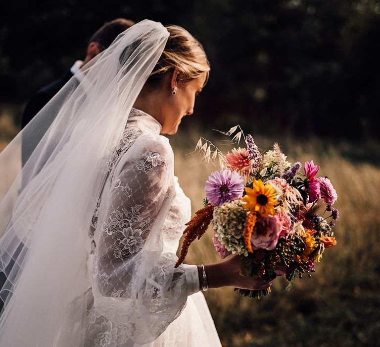 Bride in a long sleeve lace wedding dress with a veil and pink and yellow wedding bouquet 