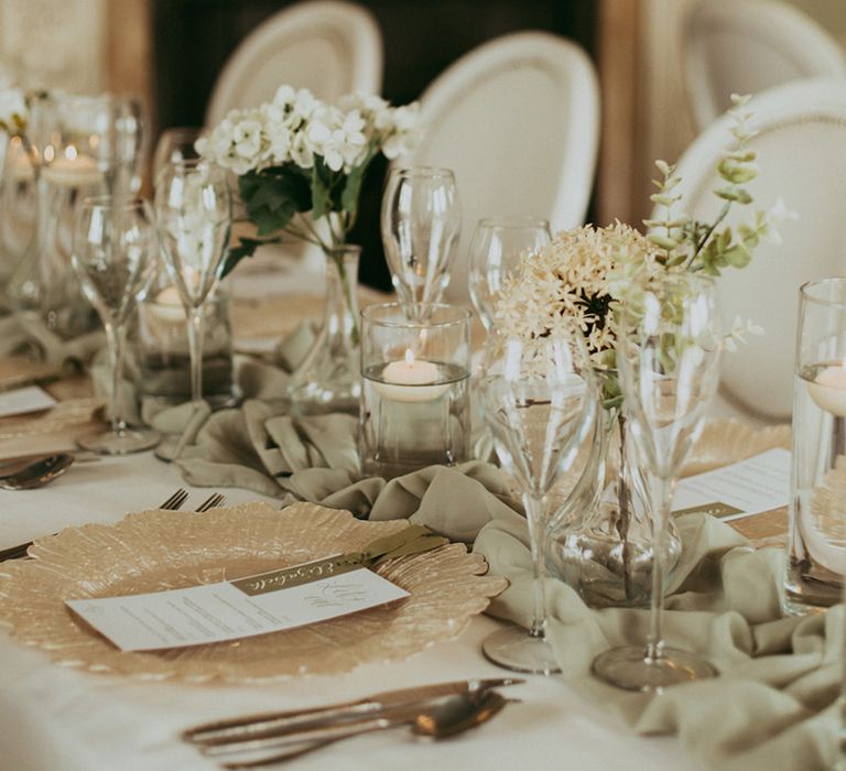 Sage green table runner with a gold charger and floating tea lights and faux wedding flowers 