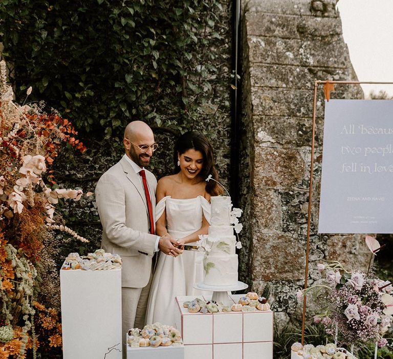 Bride and groom cut their four tier wedding cake surrounded by mini desserts and a lavender and white wedding sign 