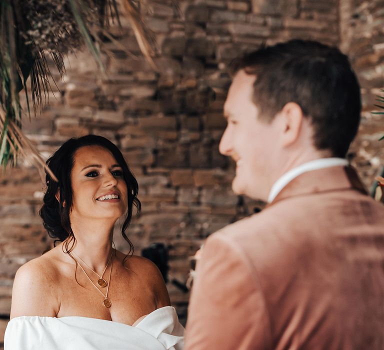 The bride wears an off the shoulder ASOS wedding dress standing at the altar with the groom 