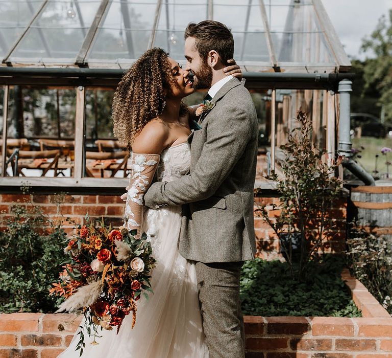 Bride in a lace and sequin off the shoulder wedding dress with the groom in a grey suit at a glasshouse reception 