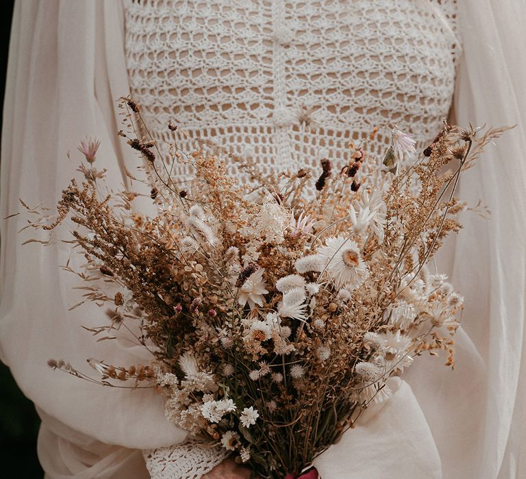 Bride holds dried floral bouquet tied with red ribbon and wears her nails painted black 