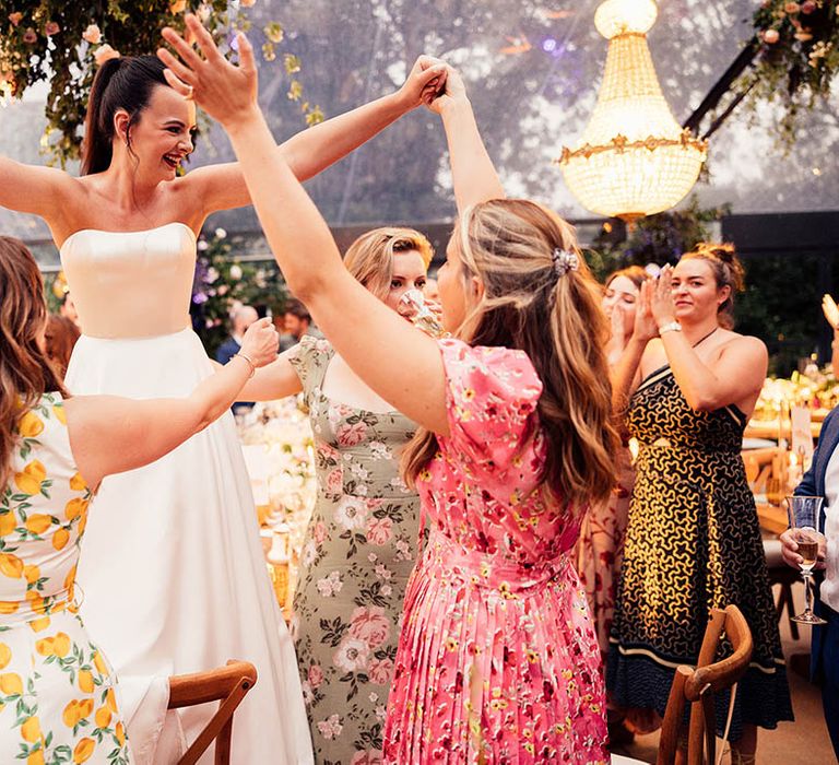 Bride dances with wedding guests fr the reception in a glass marquee 