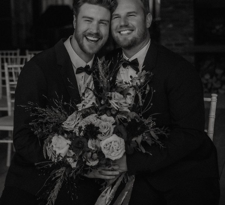 Grooms sit together with big smiles on their faces for their gay autumn wedding 