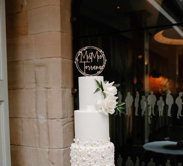 4-tier white wedding cake finished with white roses and pearl embellishment 