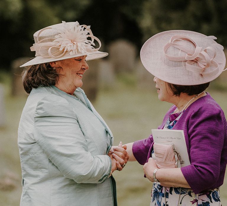 Mother of the bride in a purple blazer in a pink wedding hat greets a wedding guest for the traditional wedding 