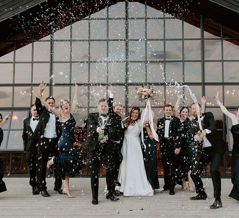 Bride & groom stand with their wedding party during champagne spray outdoors