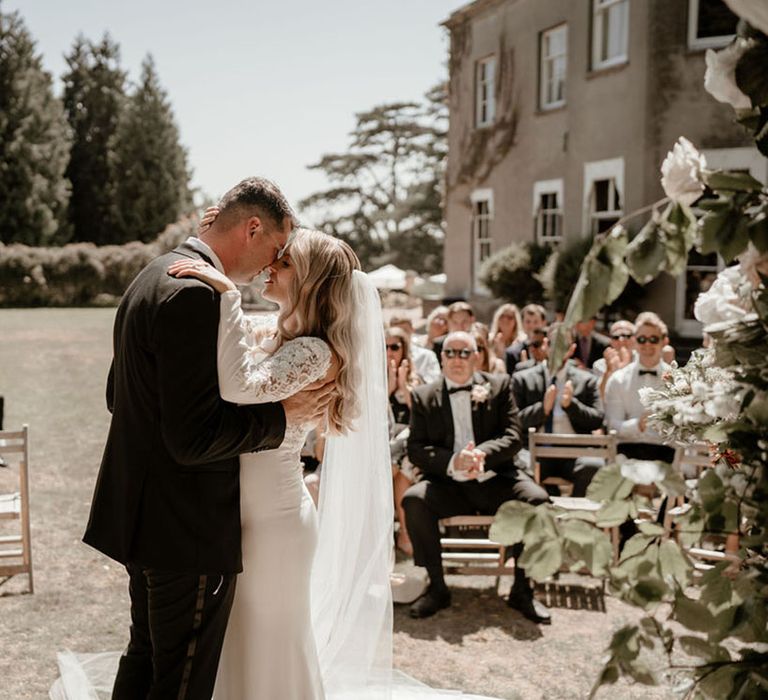 Groom in black tie leans in to kiss the bride in a long sleeve Badgley Mischka wedding dress 