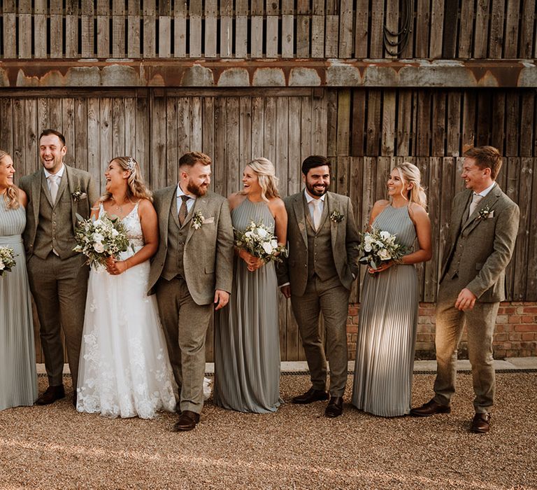 The wedding party with the groom and groomsmen in grey suits, each bridesmaid in a sage tree pleated bridesmaid dress, and the bride in a lace wedding dress