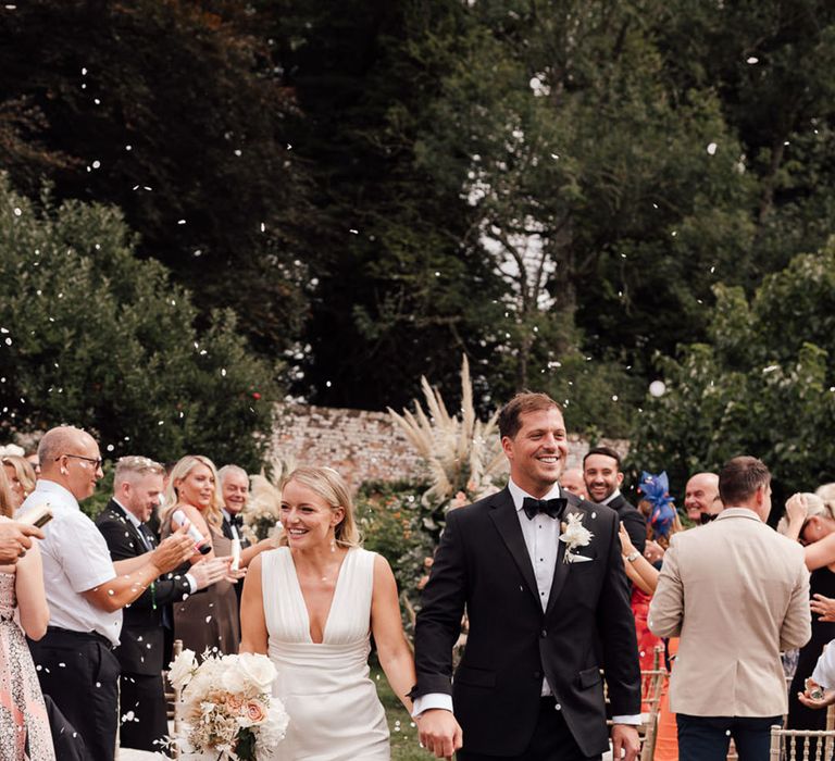 The bride and groom walk back down the aisle with confetti 