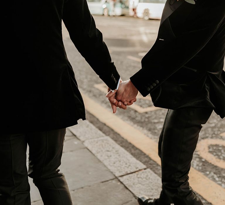 Grooms in velvet blazers and black suit trousers holding hands walking through Edinburgh after stylish city wedding