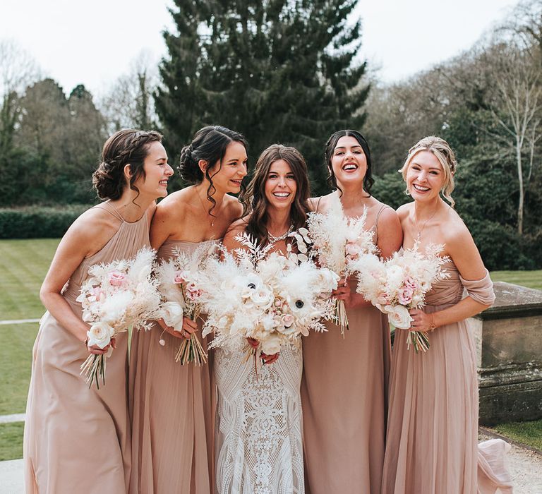 Bridal party shot with the bridesmaids wearing matching hairstyles and matching colour neutral pink dresses in different styles with the bride 