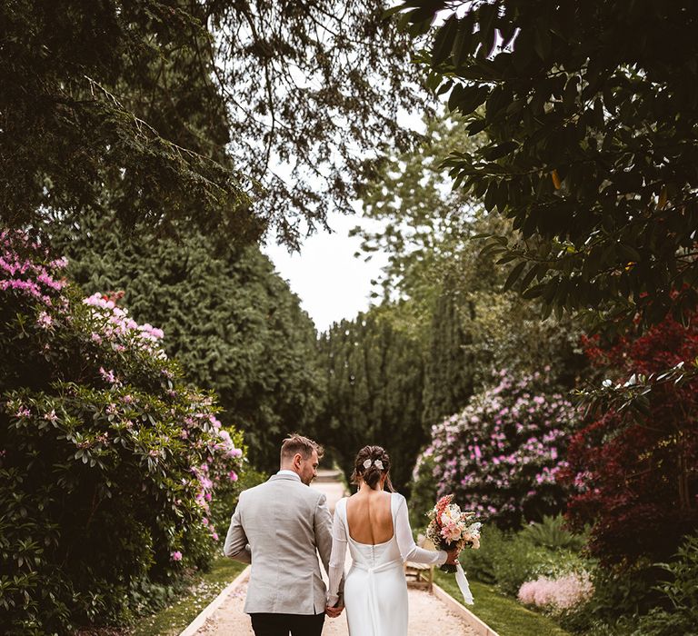 Bride in square back detail satin wedding dress and groom in grey suit and black trousers walking around the gardens of The Orangery Ingestre wedding venue