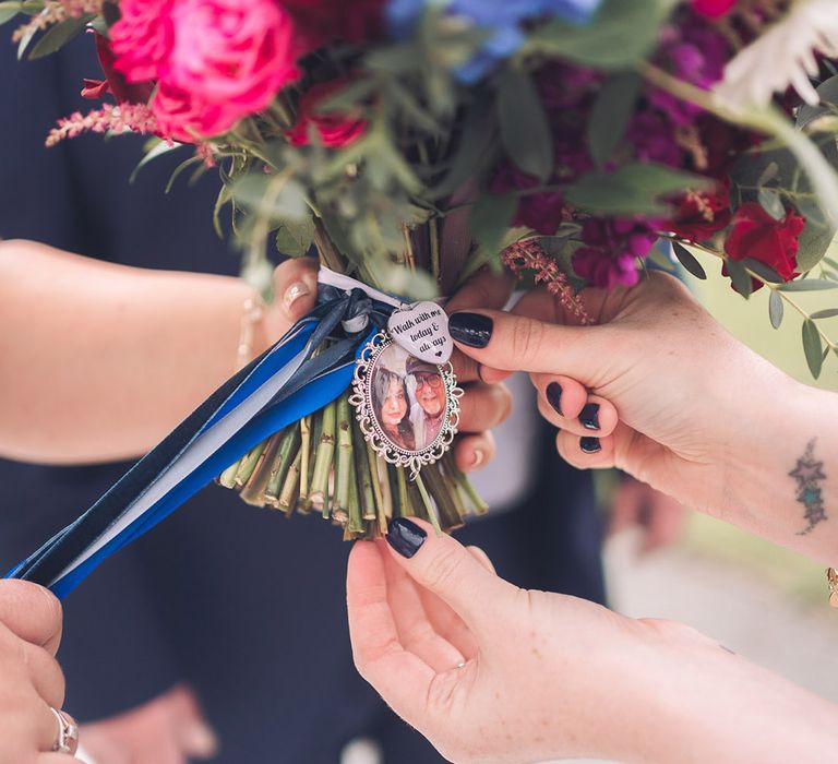 Colourful red, pink, purple, and blue wedding bouquet with personalised charm and picture of the bride and her late grandfather with blue ribbon 