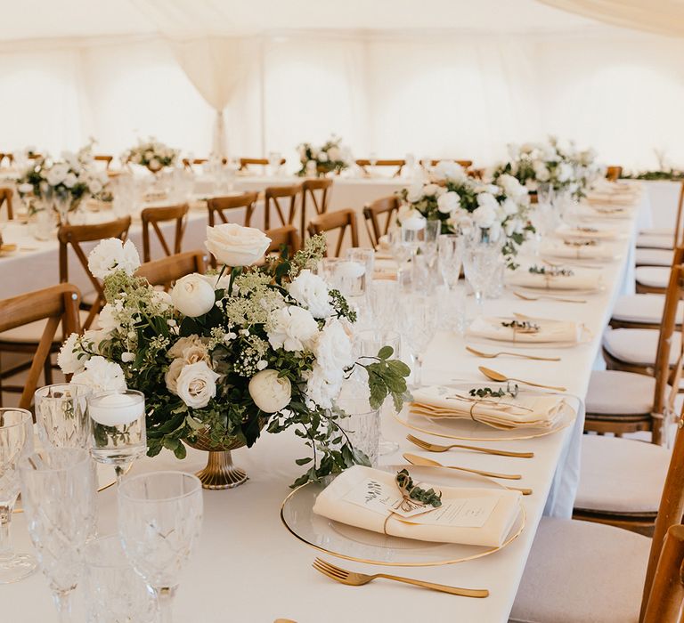 Banquet tables complete with white tablecloths, white floral arrangements and gold cutlery finished with fabric napkins tied with brown string